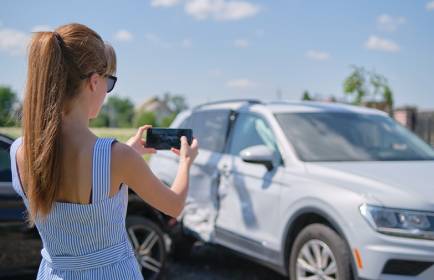 sad female driver photographing on sellphone camera wrecked vehicles on street side